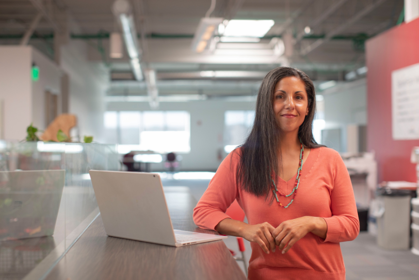 A woman stands leaning against a standing desk