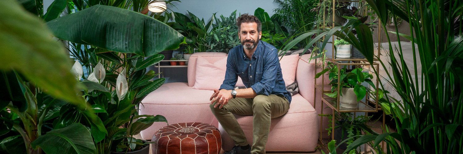 Oliver Heath sits in front of an office wall covered in green plants